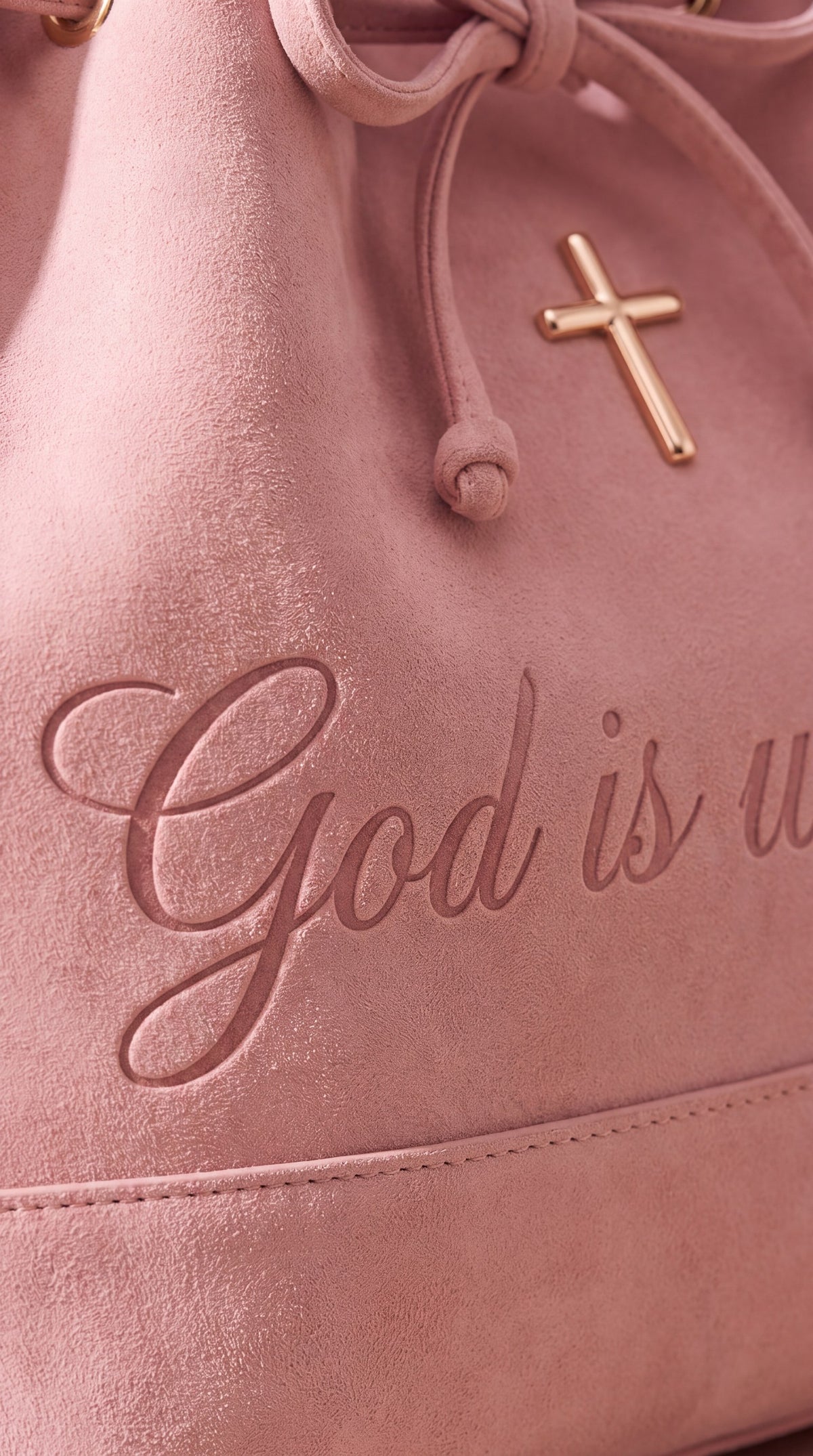 Close-up of 'God is within her' debossed on pink suede below a rose-gold cross